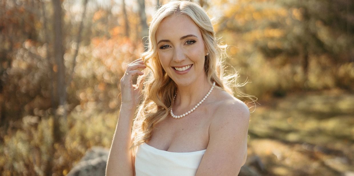Smiling bride in a white wedding dress with autumn foliage in the background.