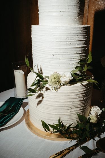 Three-tier white textured cake decorated with green leaves and white flowers.