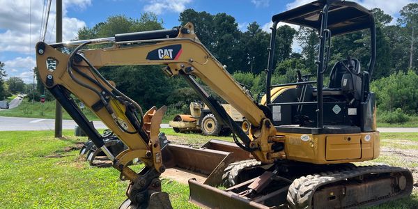 Yellow CAT mini excavator parked on grass under blue sky.