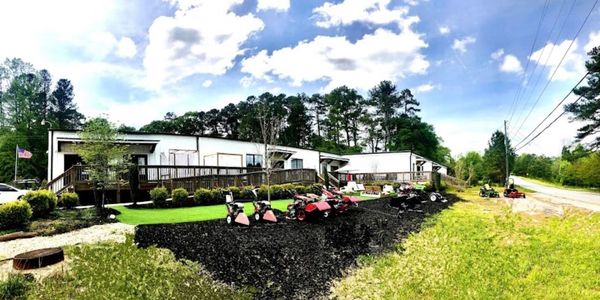 Lawn mowers displayed outside a white building on a sunny day.