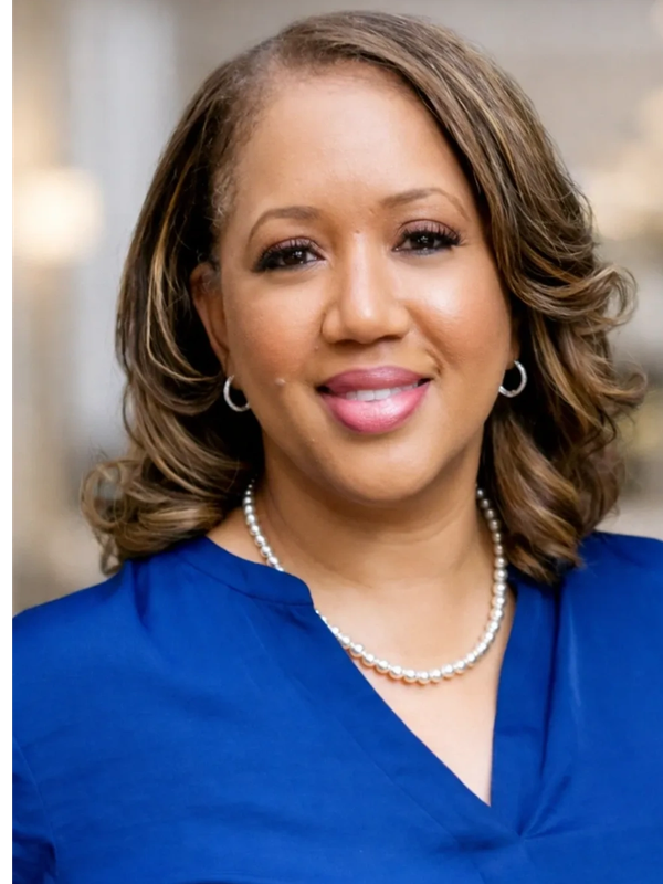 Professional woman with a warm smile in a blue top and pearl necklace.