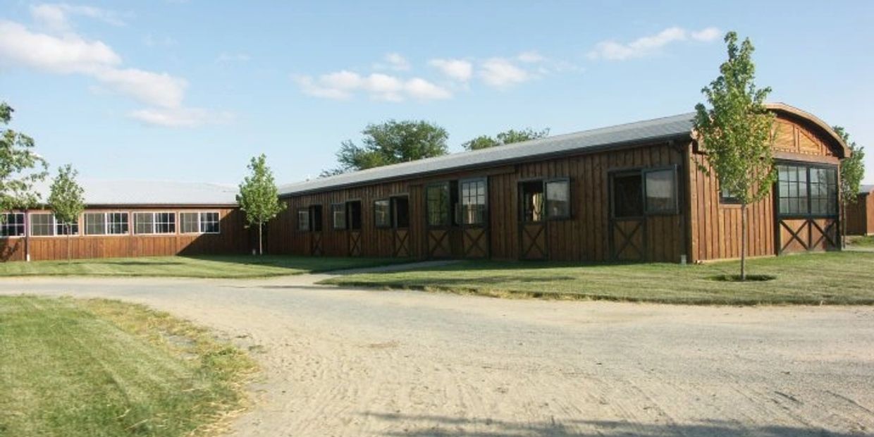 Long wooden barn-style buildings with small trees and a dirt path under a blue sky.