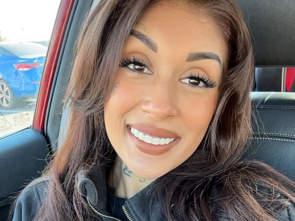 Smiling young woman with long hair wearing a black hoodie in a car.