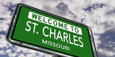 Green road sign welcoming to St. Charles, Missouri against cloudy sky.