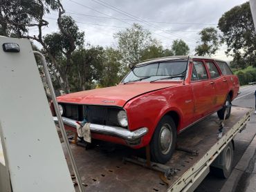 Red vintage Kingswood car on a flatbed truck.