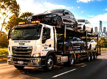 Tow truck carrying luxury cars on a highway.