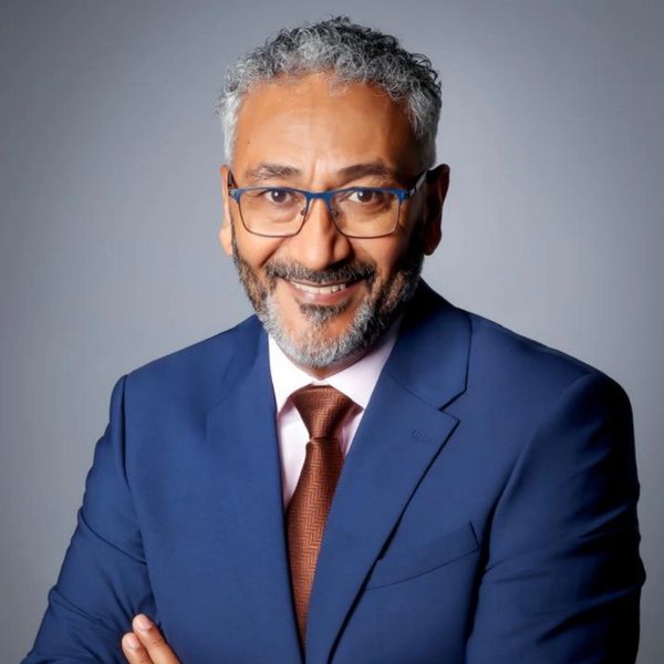 Smiling man in blue suit and glasses against a gray background.