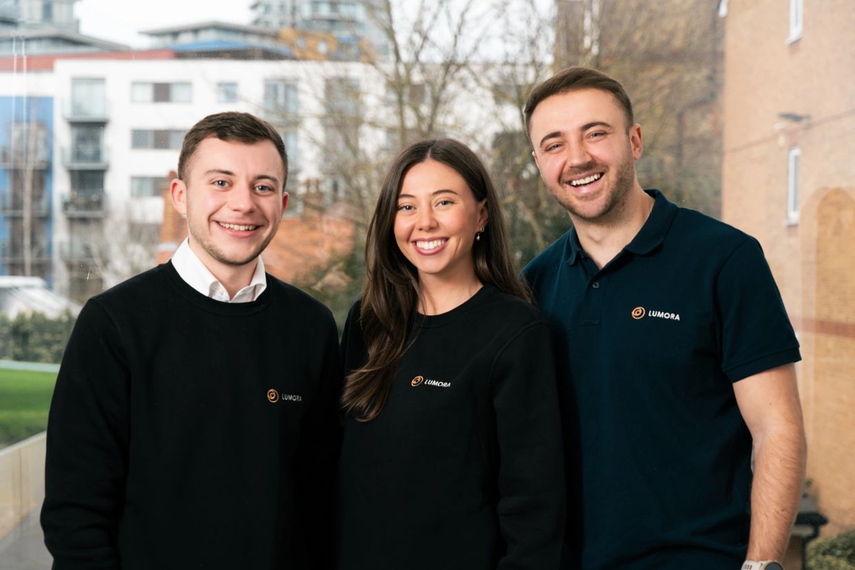 Three smiling young adults wearing Lumora branded clothing.