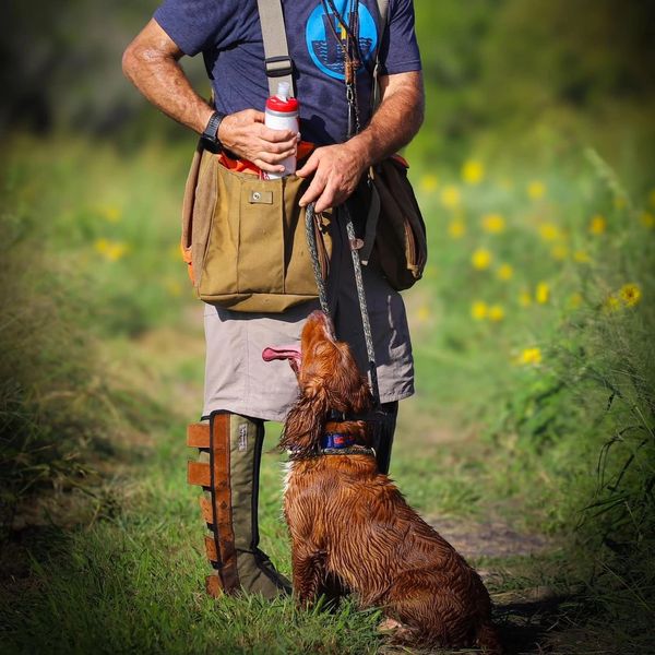 Man with a dog on a leash in a grassy area.