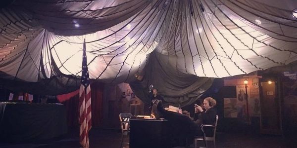 A man relaxes with feet on desk under a parachute indoors beside a U.S. flag.