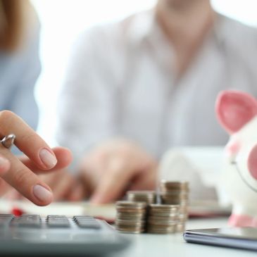 Person using a calculator with stacked coins and a piggy bank nearby.
