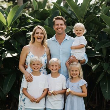 Happy family of six posing outdoors with tropical greenery in the background.
