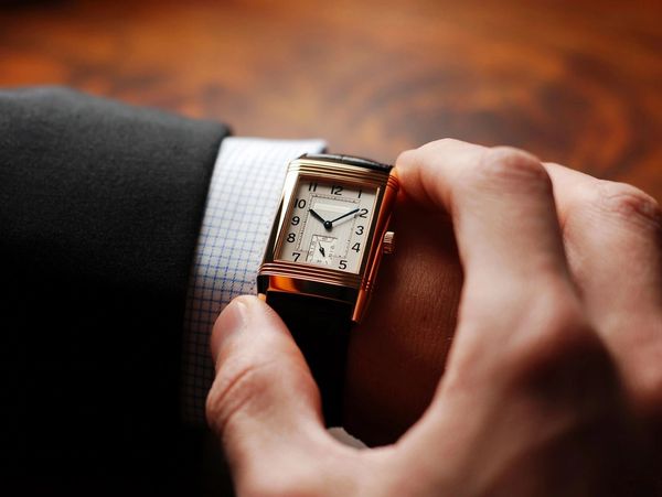 A hand adjusts a vintage-style watch on a suited wrist, showcasing a classic design