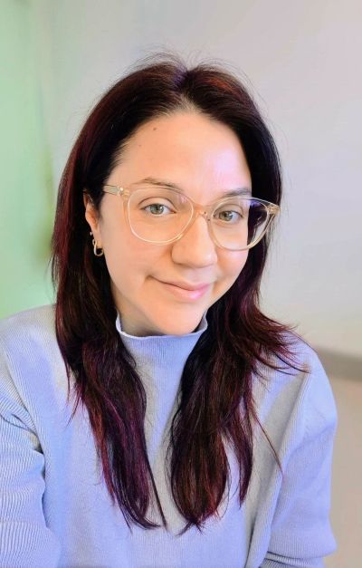 Femme souriante avec lunettes transparentes et pull violet.