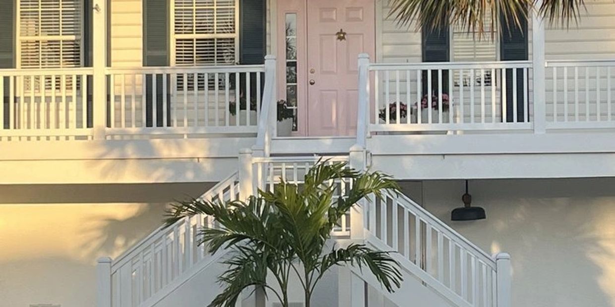 A white house with a pink door and large palm tree in front.