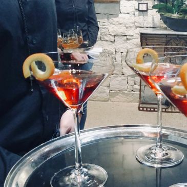 Martini glasses with orange peel garnish on a tray held by a waiter.