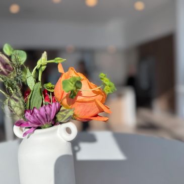 A small white vase holding colorful flowers on a table.
