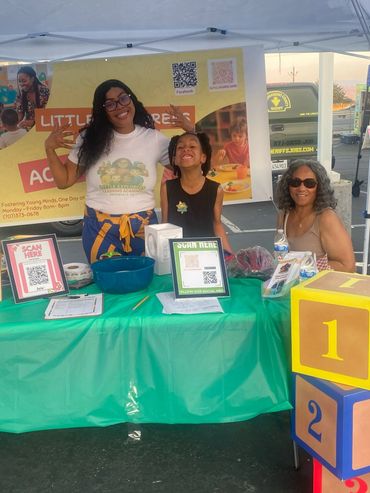Three smiling people at a colorful educational booth with large numbered blocks.