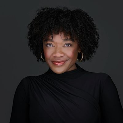 Confident woman with natural curly hair smiles warmly against a dark background.