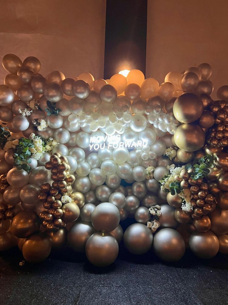 A decorative balloon wall with gold, silver, and white balloons and flowers.