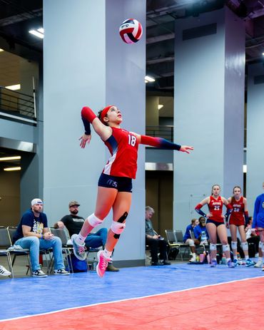 Volleyball player in mid-air preparing to serve the ball during a match.
