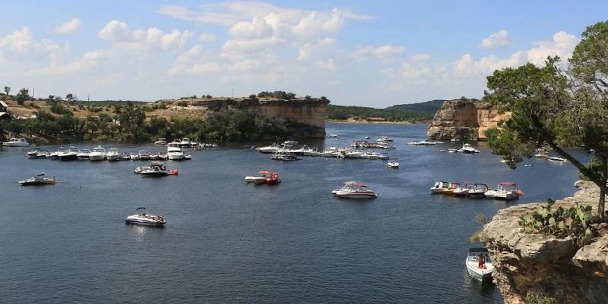 Boats anchored in a scenic lake surrounded by rocky cliffs and greenery under a partly cloudy sky.