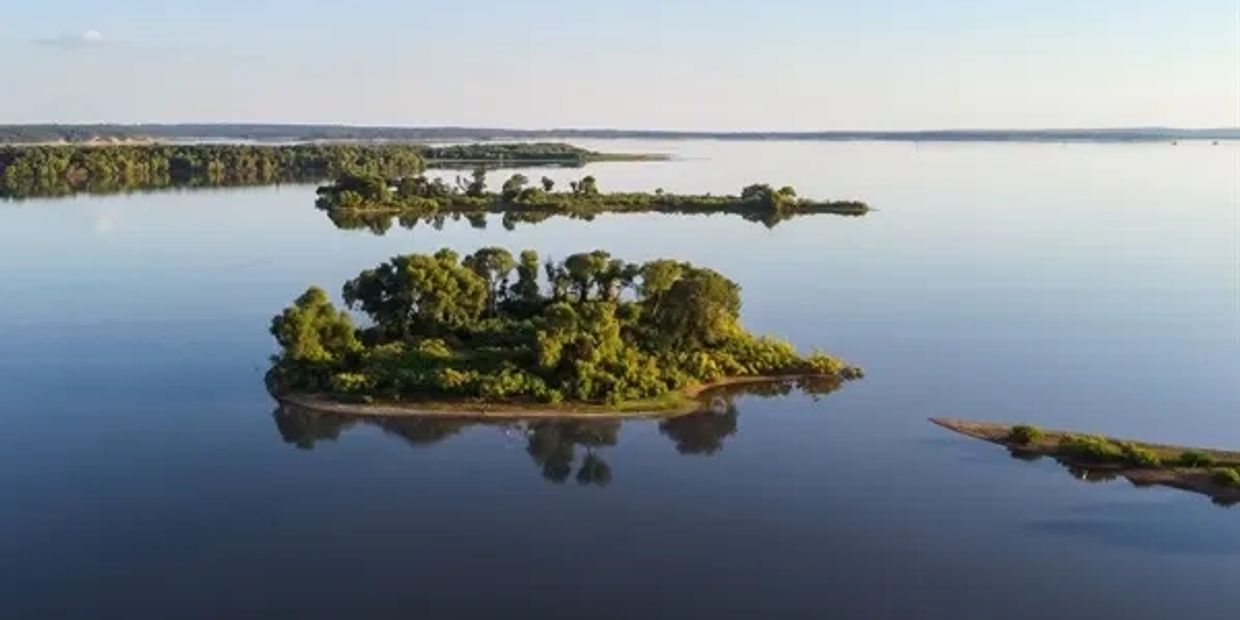 Calm lake with small green islands under clear sky.