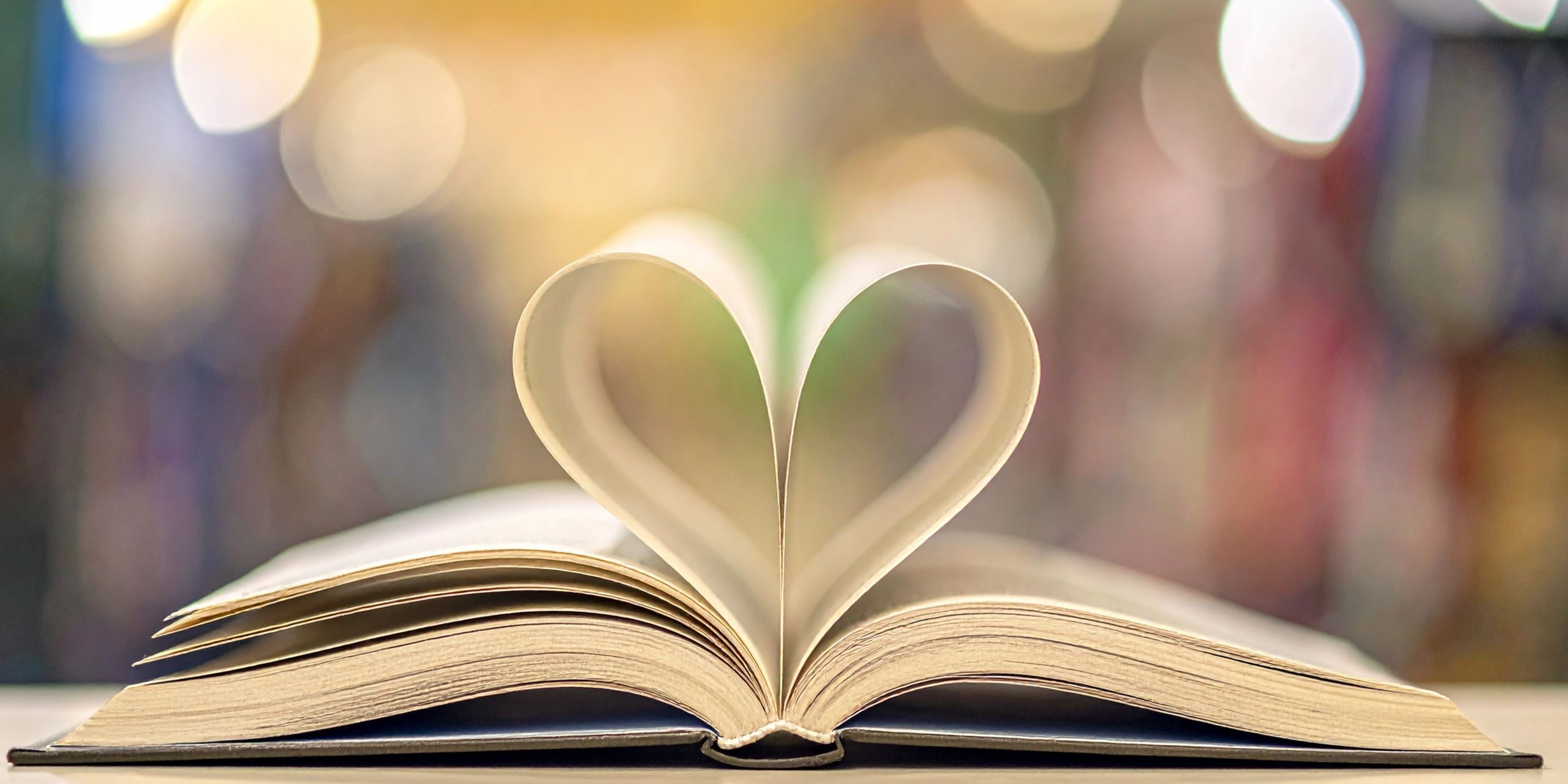 Book pages folded into a heart shape with soft bokeh background.