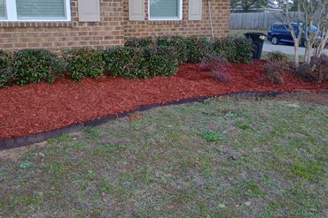 Freshly mulched garden bed with shrubs along a brick house.