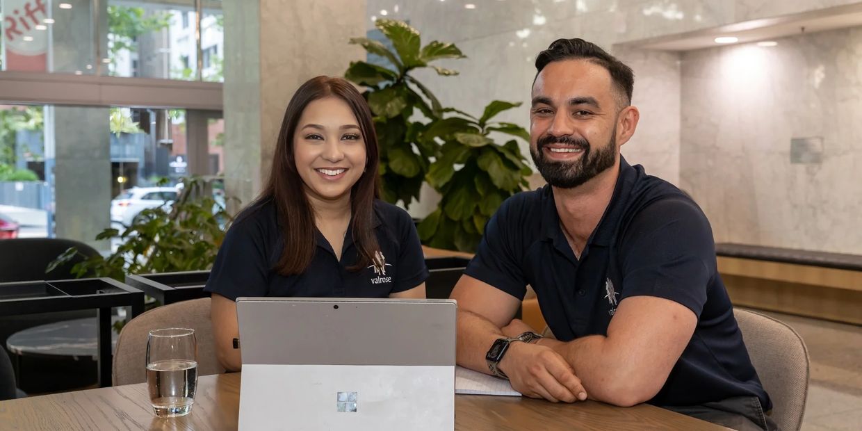 Two smiling Valrose team members sitting at a table in a modern office space, collaborating