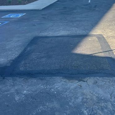A freshly repaired square area on cracked pavement in a parking lot completed by Integrous Paving.