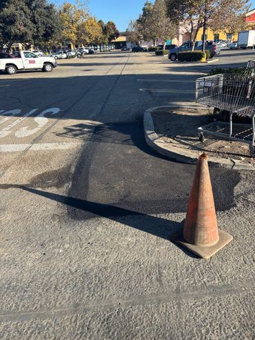 Fresh asphalt repair completed by Integrous Paving beside a commercial building and curb.