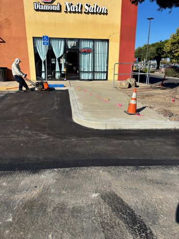 Fresh asphalt repair completed by Integrous Paving beside a commercial building and curb.