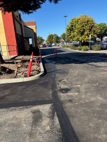 Fresh asphalt repair completed by Integrous Paving beside a commercial building and curb.