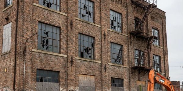 Abandoned brick building with shattered windows and rusty fire escape.