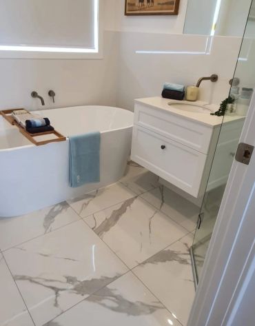 Modern white bathroom with marble floor, tub, and vanity.