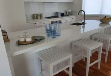 Modern kitchen with white stools and countertop.