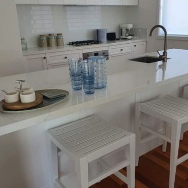 Modern white kitchen with island, blue glasses, and wooden stools.