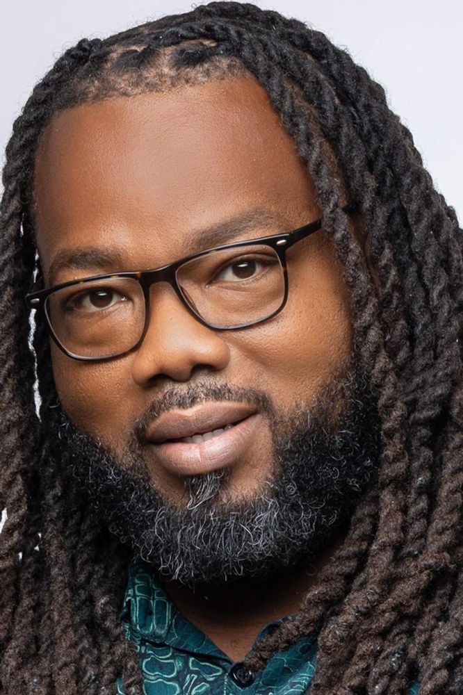 Bahamian man with dreadlocks and glasses smiling confidently.