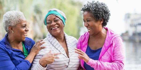 Three older women laughing and enjoying each other's company outdoors.