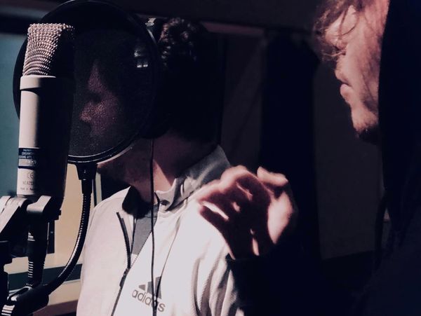Two men in a recording studio, one singing into a microphone.
