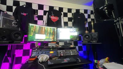 Audio workstation with dual displays, studio monitors, acoustic panels, and purple lighting.