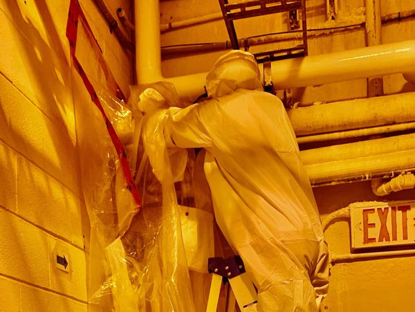 An inspector on a ladder searching for asbestos within pipes.