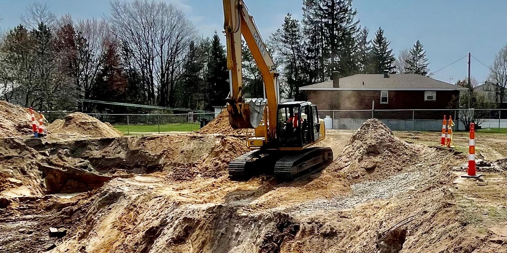 A giant hole behind a house being dug by an excavator.