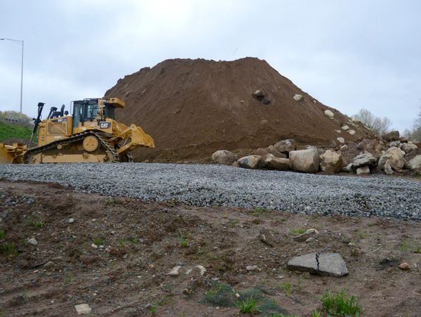 A hill of dirt with rocks at the base and an excavator in front of it.