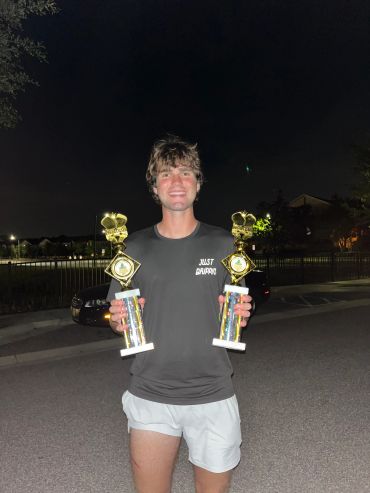 Man holding two trophies and smiling at night.