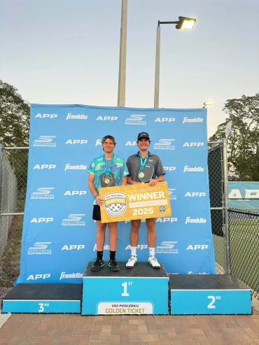 Two pickleball winners holding a golden ticket on the winner's podium.