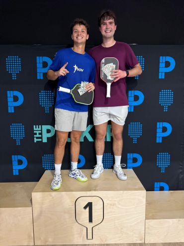 Two men holding paddles and cash on a winners' podium.