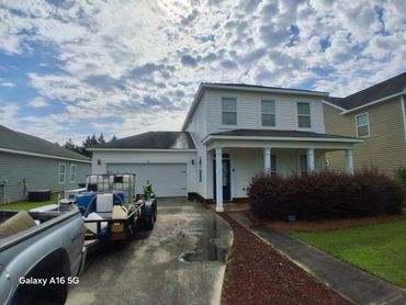 Two-story house with a truck and trailer parked in the driveway under a cloudy sky.