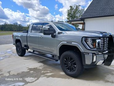 Silver GMC Denali HD pickup truck parked on a driveway under a blue sky.
